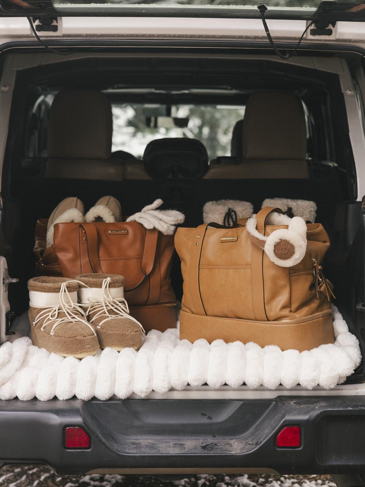 Trunk of a car with brown boots and travel bags on a white blanket