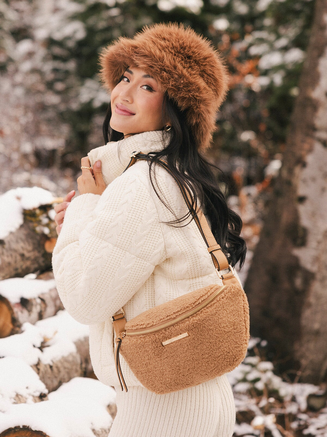 Woman in a snowy landscape wearing a fur hat and a brown faux fur bag.
