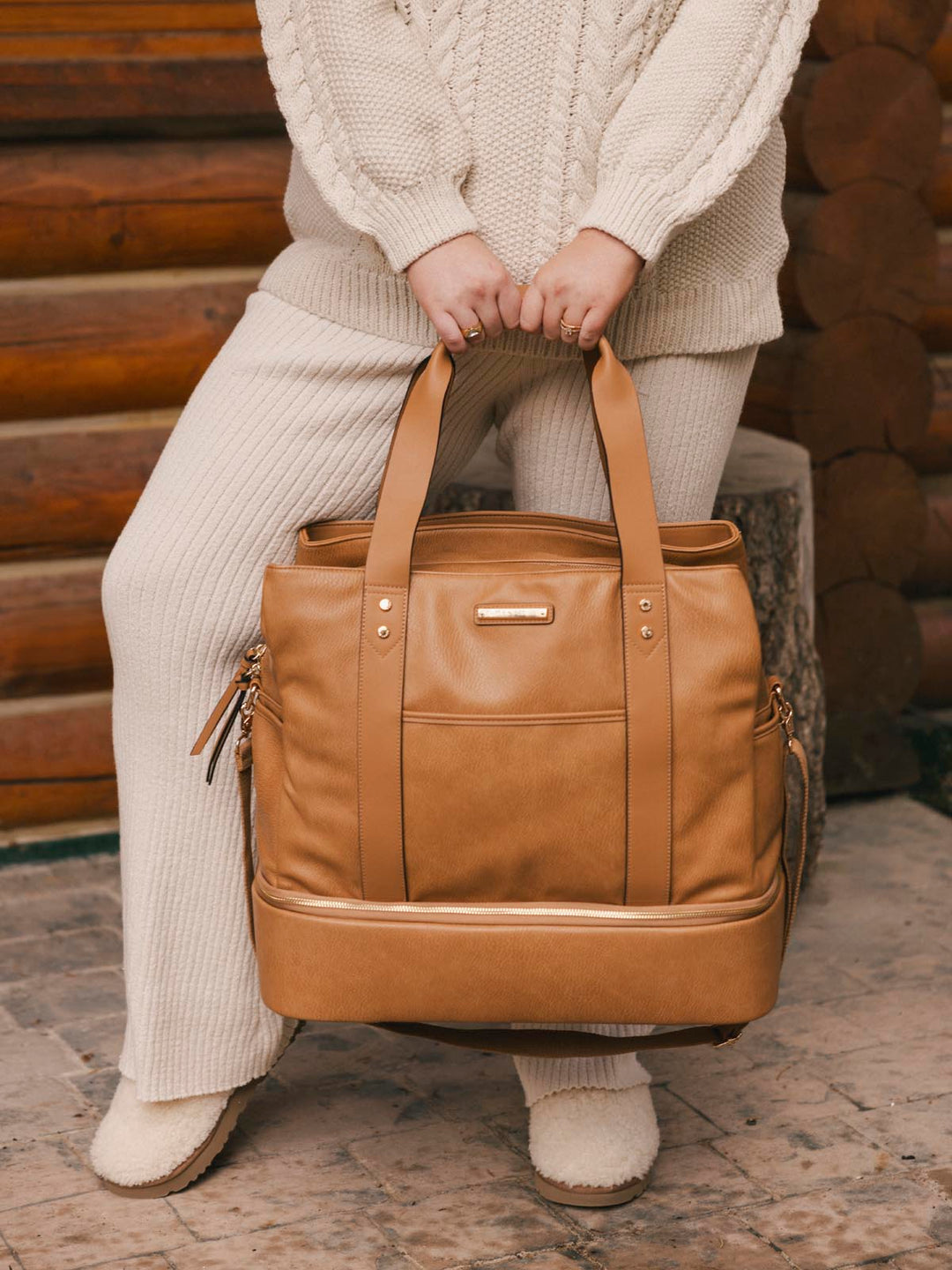 Person holding a brown leather bag in front of a wooden background