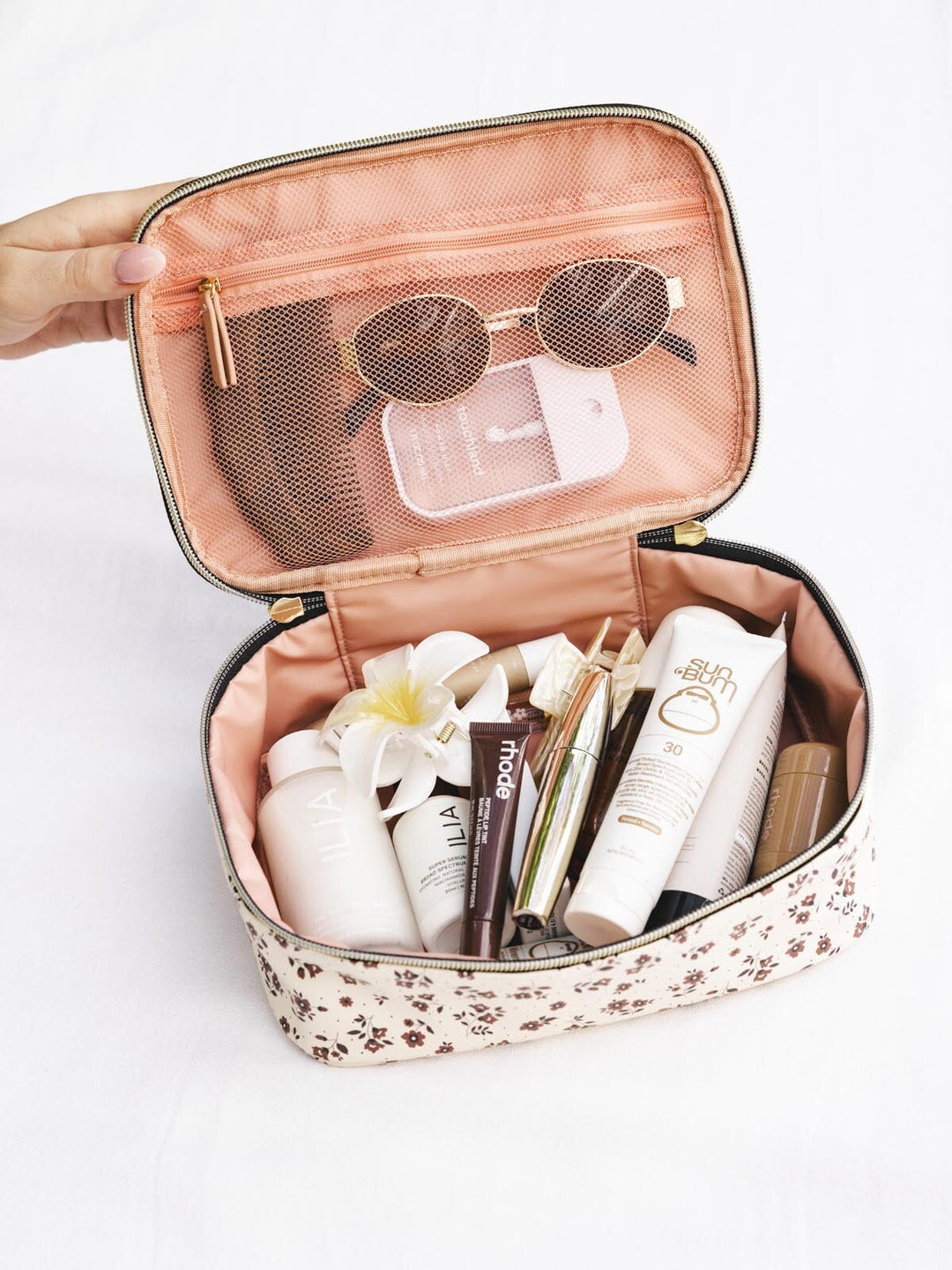 Brown floral travel case with toiletries and sunglasses in it.