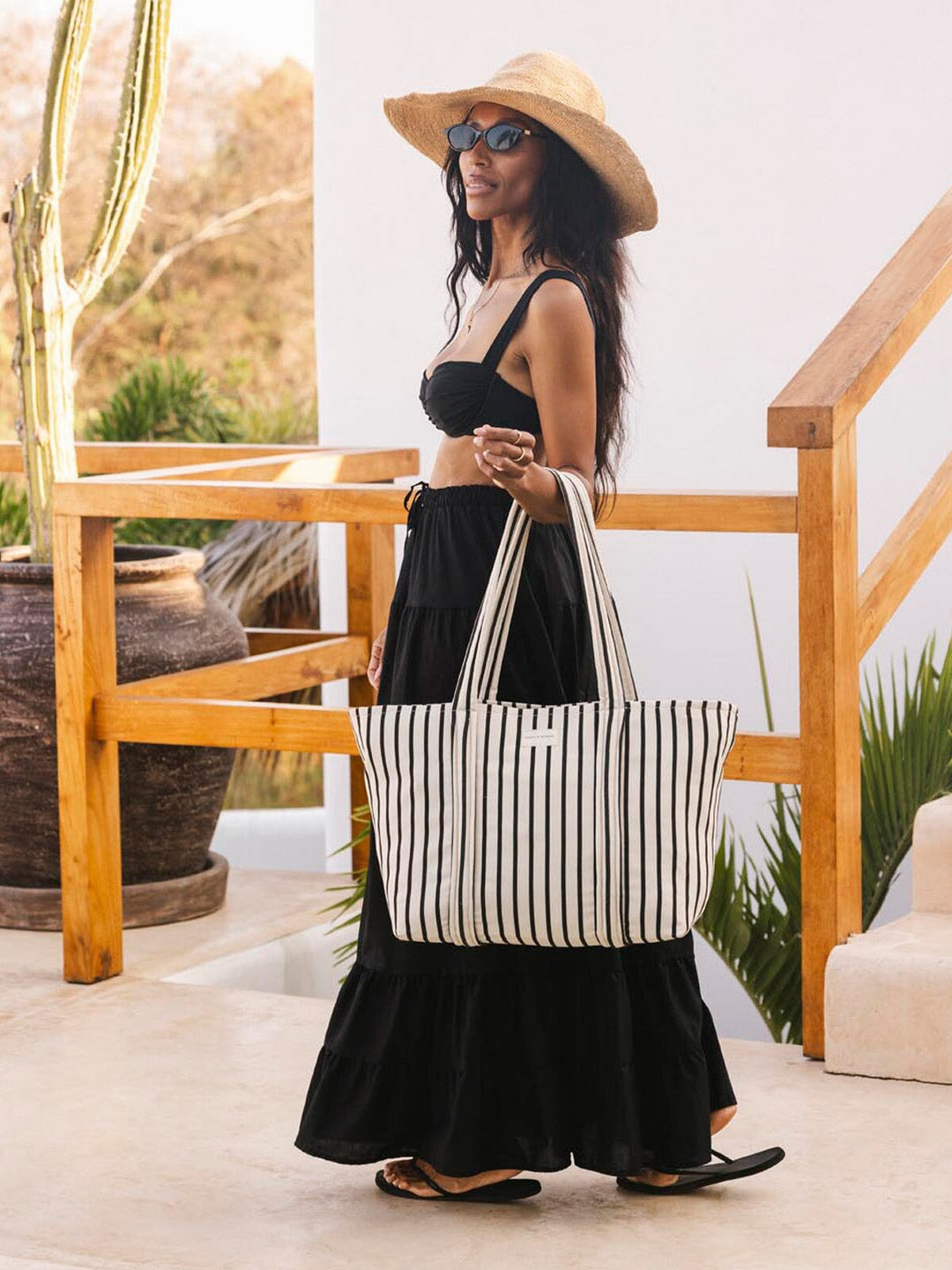 Woman holding a striped tote bag on a wooden deck with plants in the background