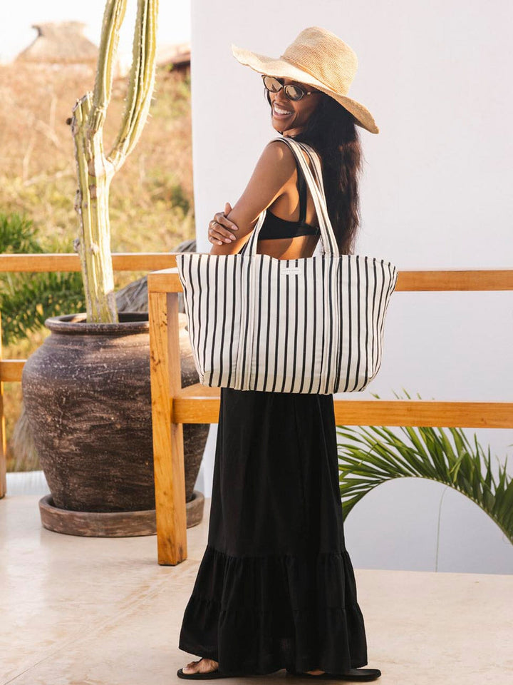 Woman holding a striped tote bag on a patio with plants and a pot in the background