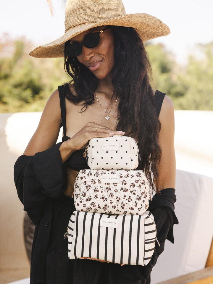Woman holding a stack of three small cosmetic bags outdoors