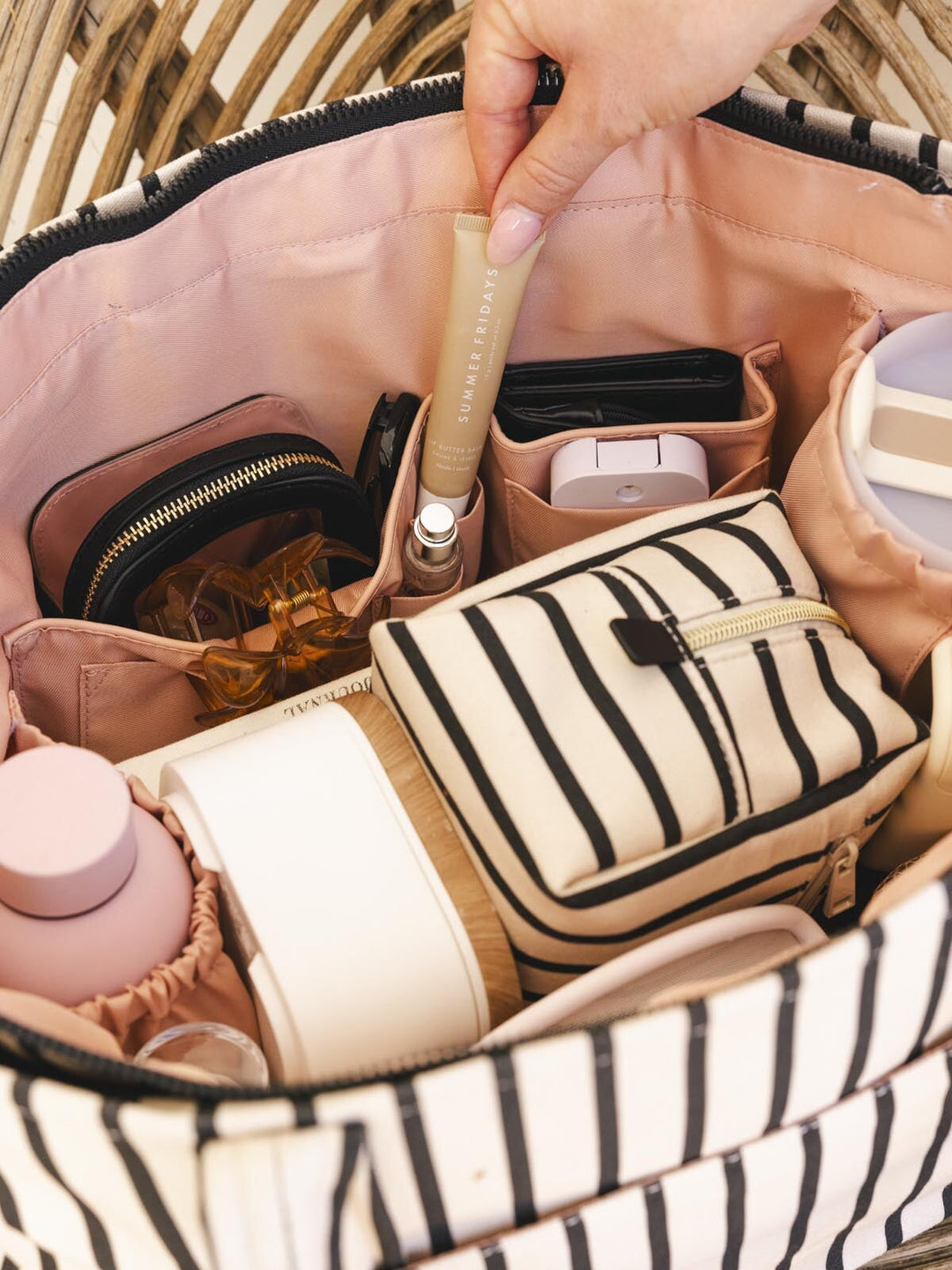 Person pulling a lip balm out of a striped tote bag