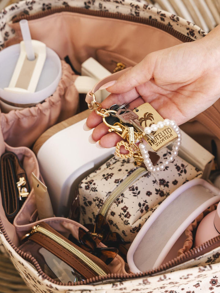 Hand holding a keychain with a palm tree design over an open bag containing various items.