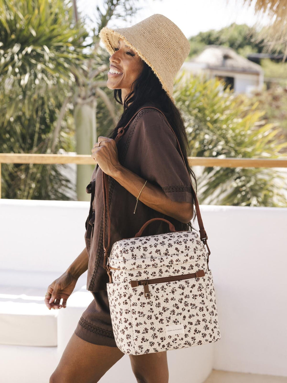Woman with a floral-patterned lunch bag with brown straps and sun hat in a tropical setting