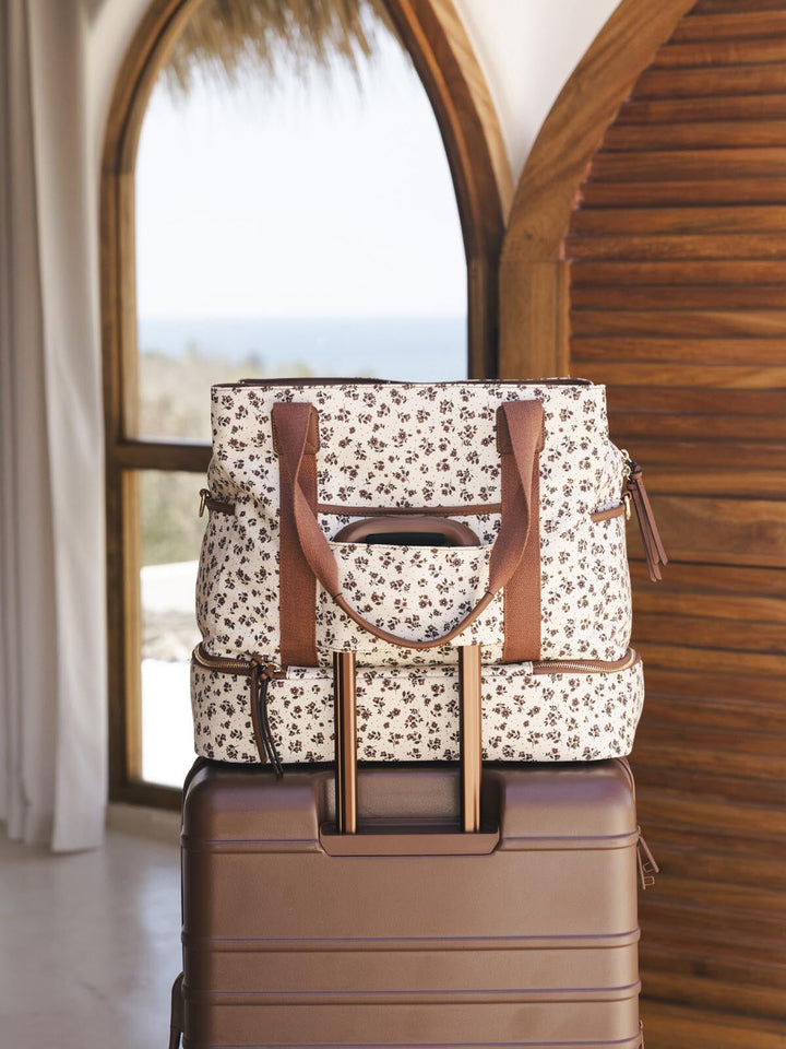 Floral-patterned travel bag with brown straps on top of a brown suitcase