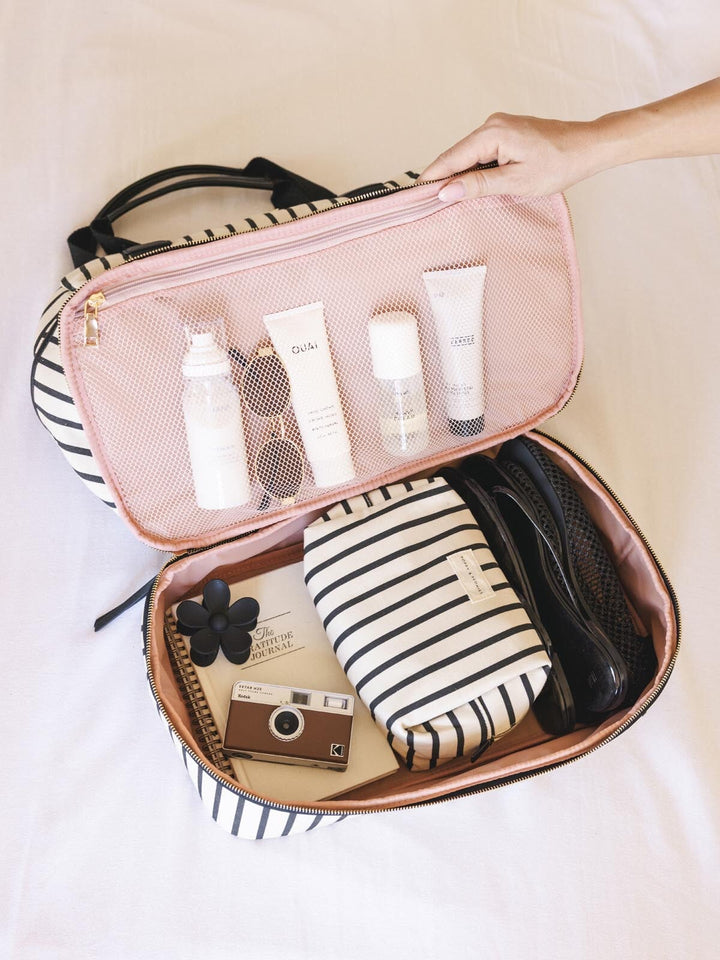 Open travel bag with toiletries and a camera on a light background