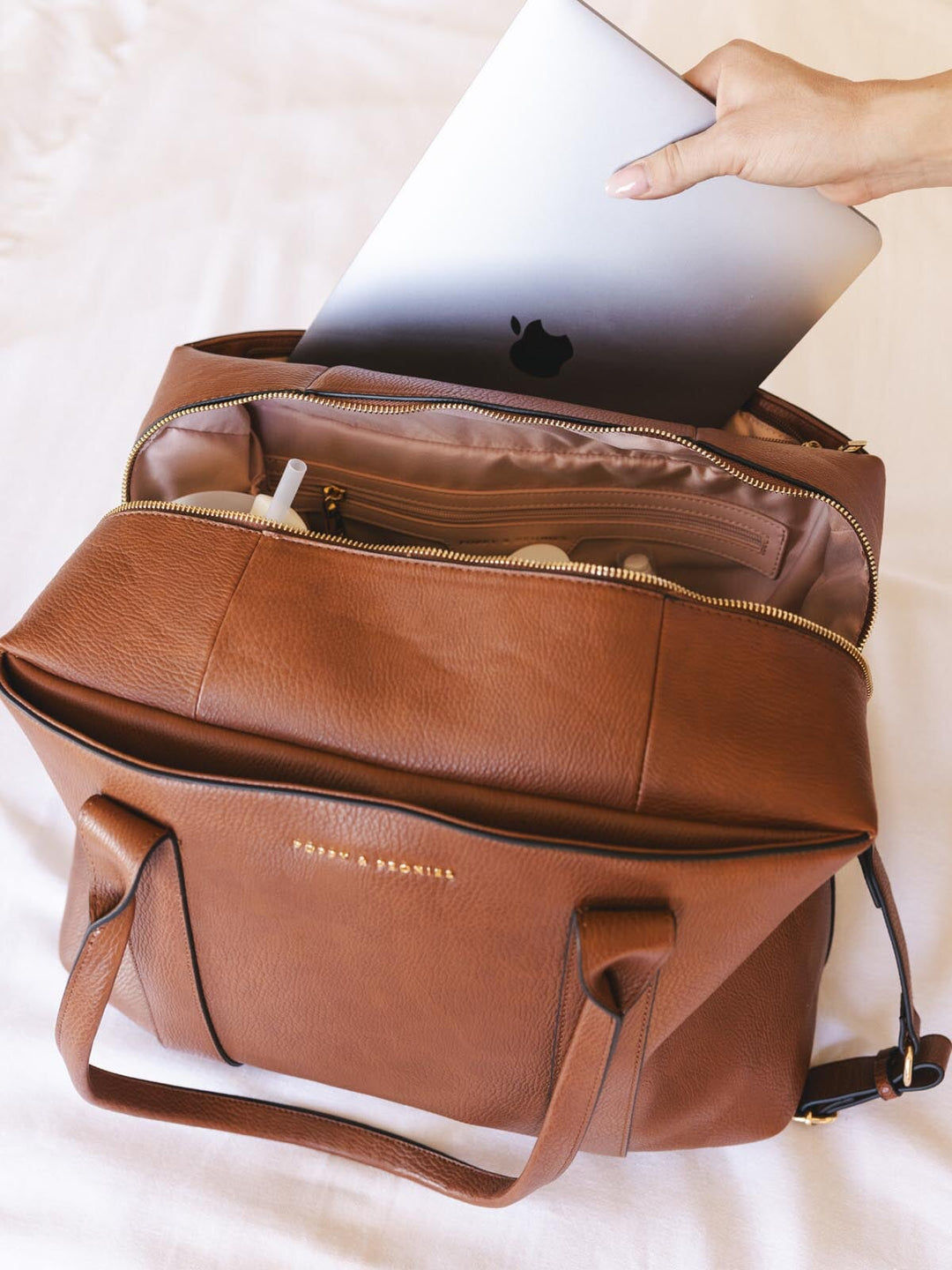 Brown vegan leather bag with a laptop being placed inside on a light background