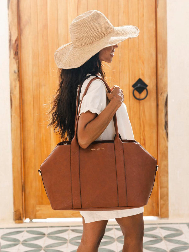 Woman wearing a large straw hat and holding a brown vegan leather bag against a wooden door background