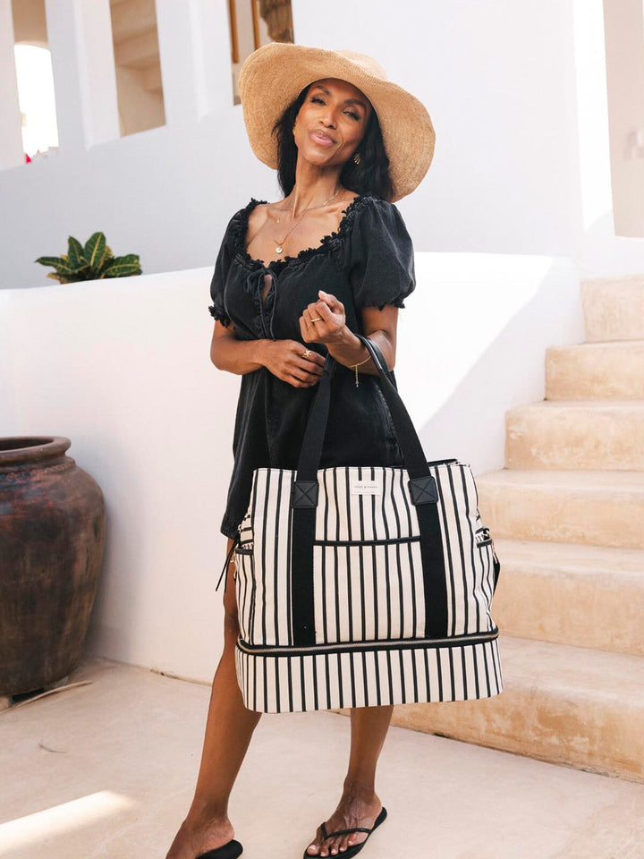 Woman holding a black and white striped travel bag in an outdoor setting