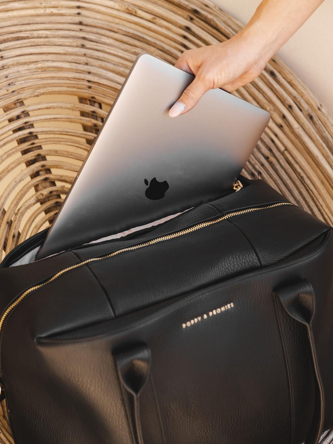 Person placing a silver laptop into a black vegan leather duffle bag