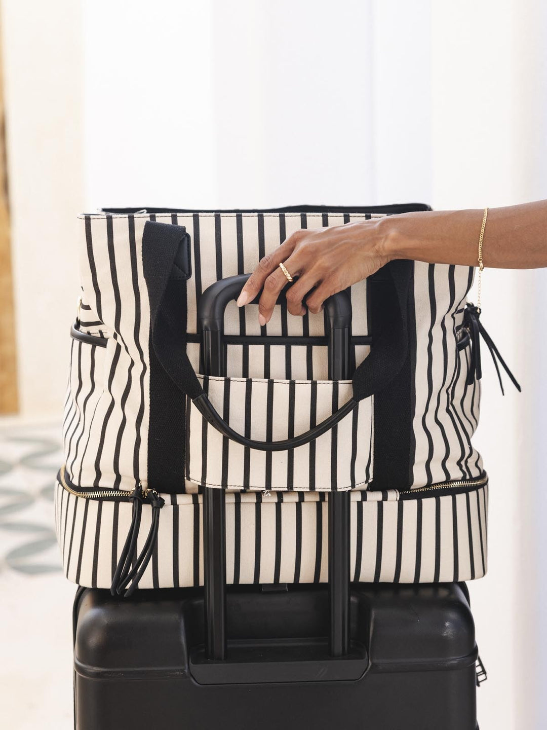 Person holding a black and white striped tote bag over a suitcase.