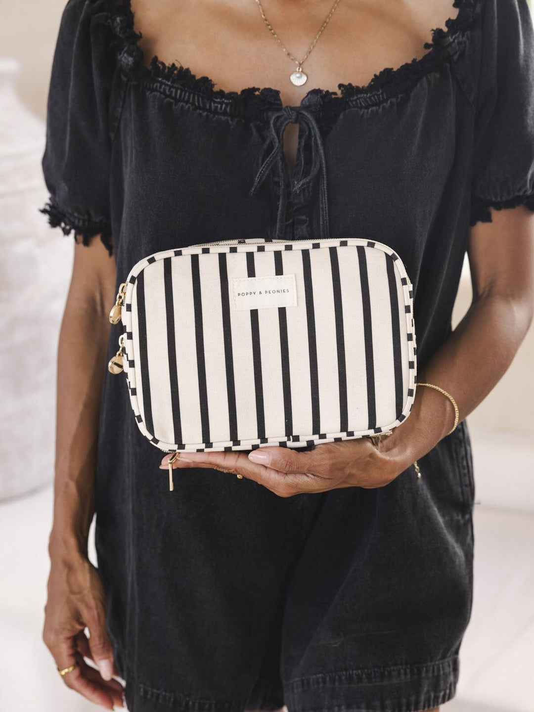 Person wearing black holding a black and white striped pouch.