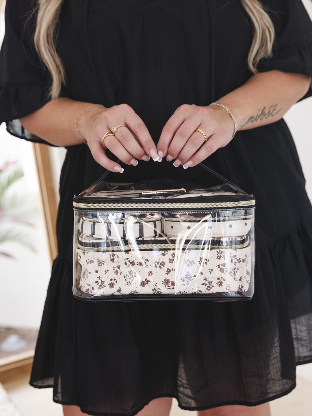 Person holding a clear makeup bag with floral and stripe pouches inside.