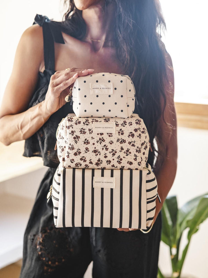 Woman holding a stack of three patterned cosmetic bags.