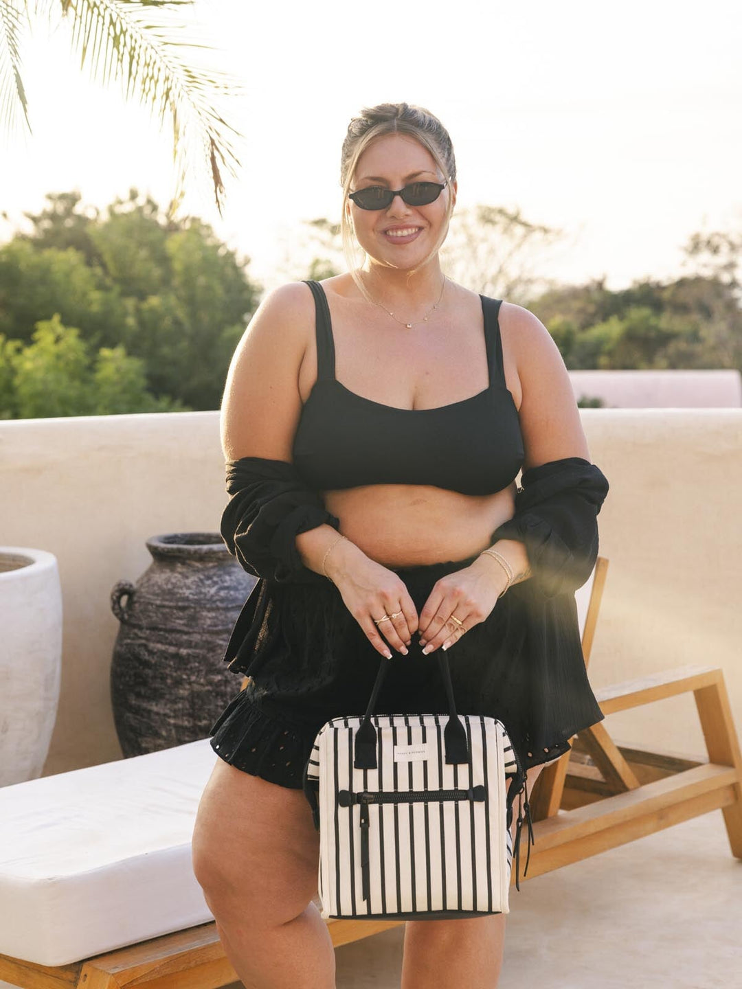 Woman in black outfit holding a striped lunch bag