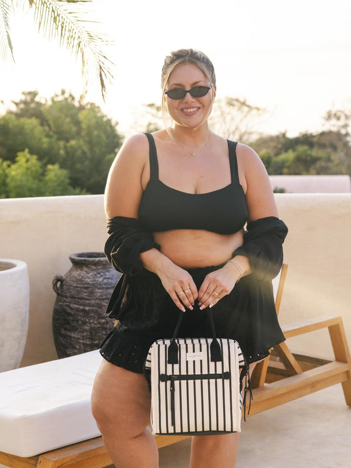 Woman in black outfit holding a striped lunch bag