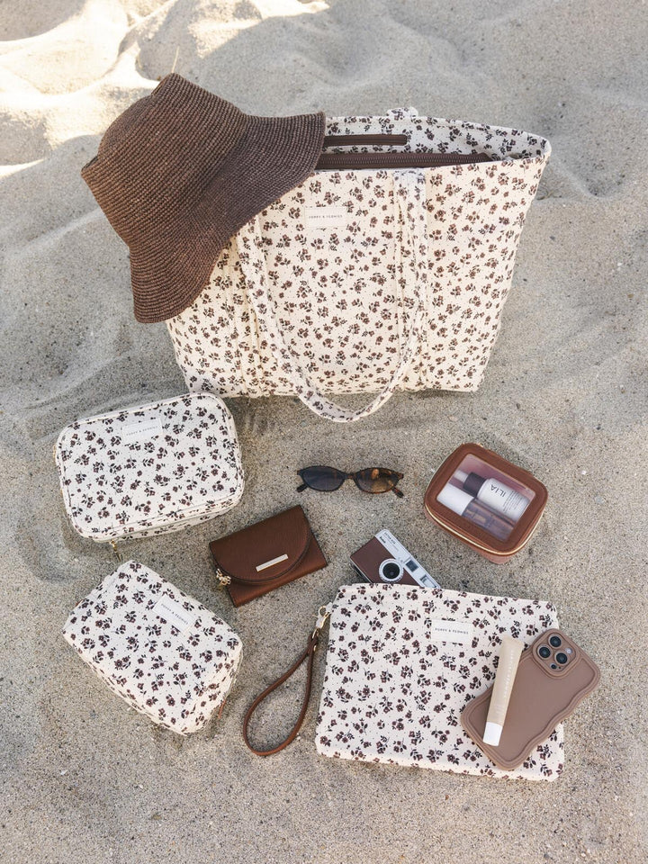 Collection of floral-patterned bags and accessories on a sandy surface
