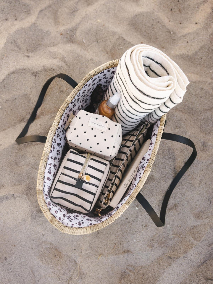 Open straw tote bag with a towel and cosmetic bags inside.