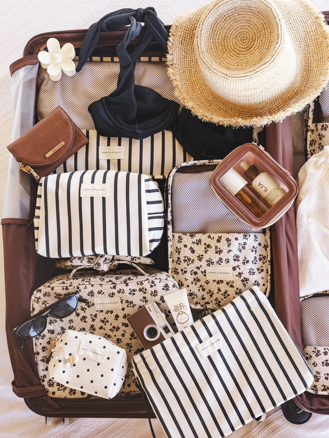 Open suitcase with various travel items including a hat, sunglasses, cosmetic bags and packing cubes.