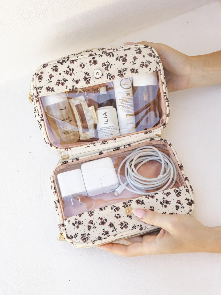 Floral-patterned travel case with toiletries and electronic items on a white background