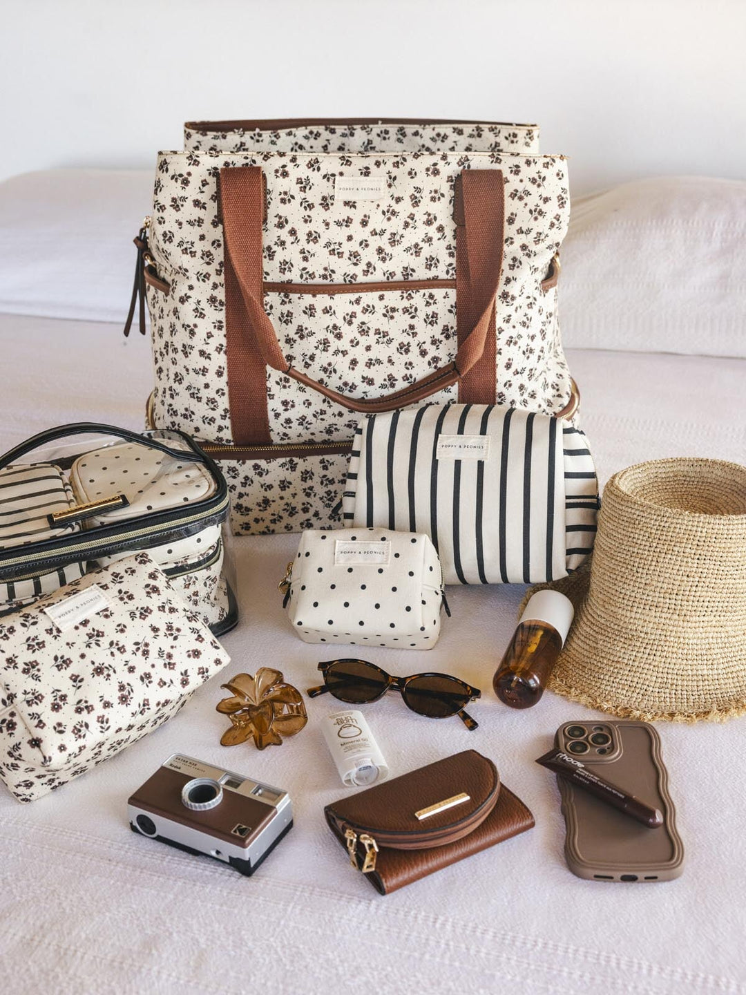 Collection of bags, sunglasses, camera, and phone on a white surface with a floral-patterned travel bag as the focal point.