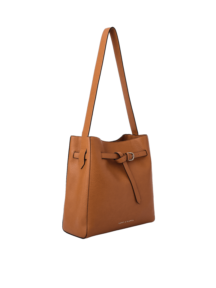 Poppy & Peonies The Knot Shoulder Bag in Cognac, shown from a three-quarter angle highlighting its slim rectangular silhouette, decorative belted buckle, gold-tone hardware, and long shoulder strap.