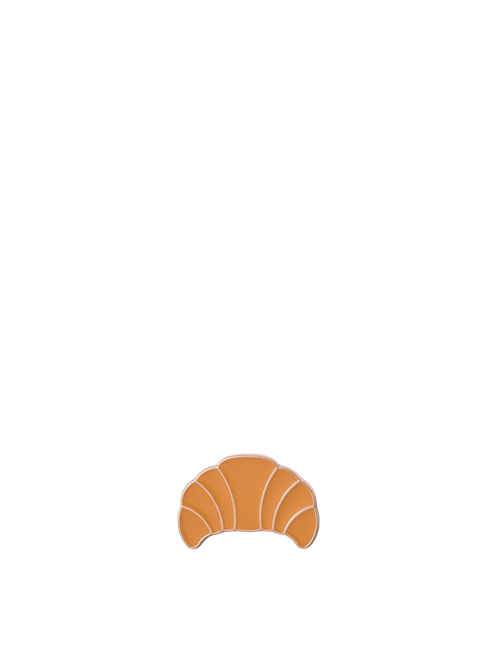 Poppy & Peonies Enamel Pin featuring a golden-brown croissant with curved detailing.