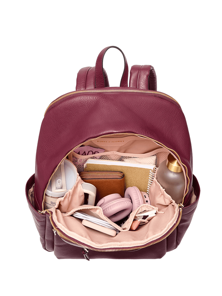 Open berry coloured backpack with various items on a transparent background