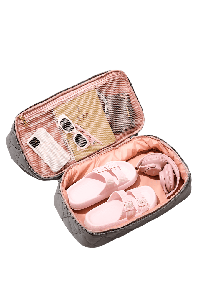 Open travel pouch containing pink shoes, sunglasses, and a phone on a green background