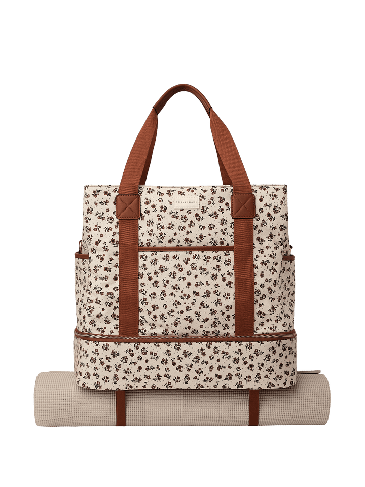 Floral-patterned travel bag with brown straps and a yoga mat attached to the bottom