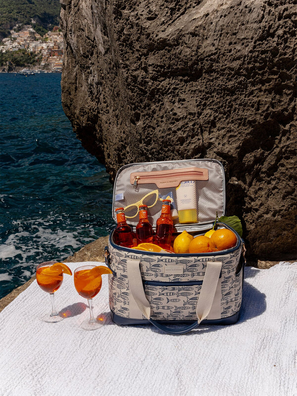Open sardine printed cooler bag with drinks and snacks by a rocky coastline