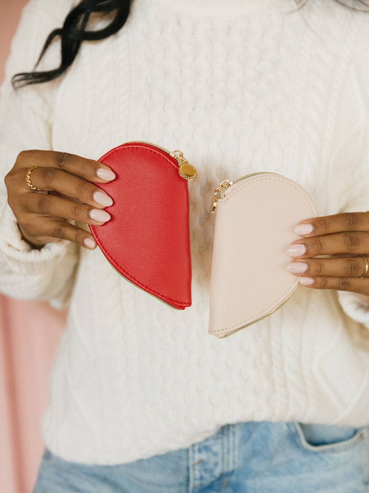 Two heart-shaped pouches, one red and one beige, held by a person wearing a white sweater.