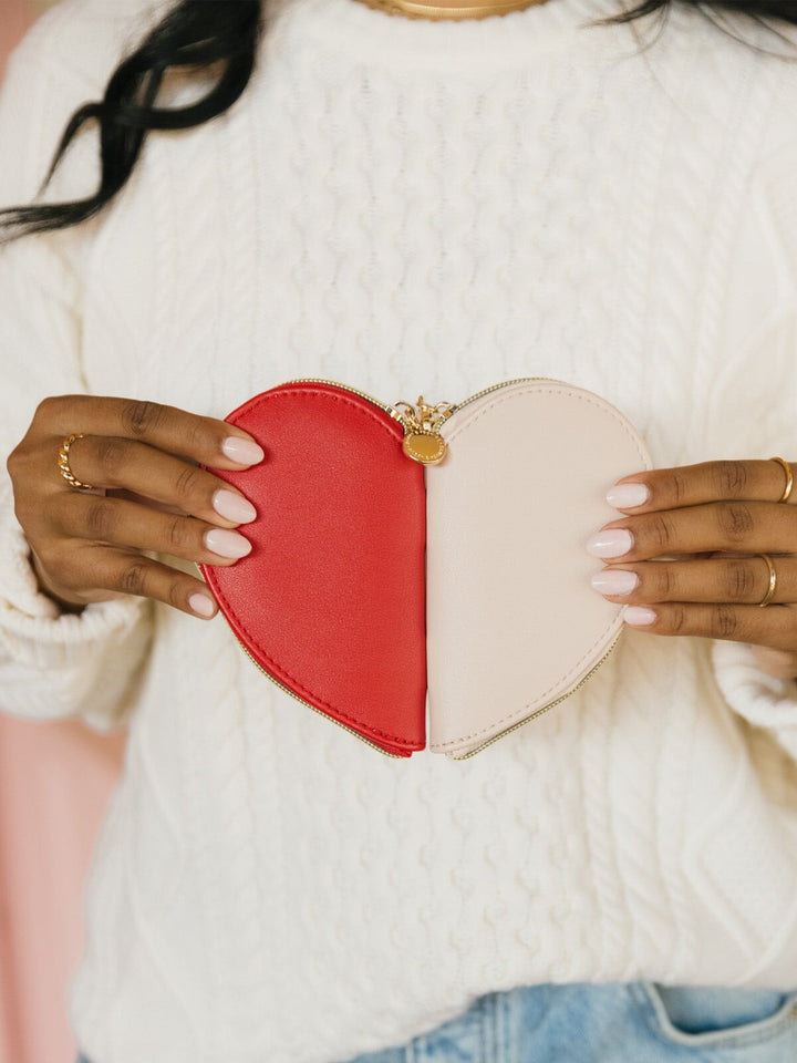 Heart-shaped red and pink coin pouch held by a person wearing a white sweater.