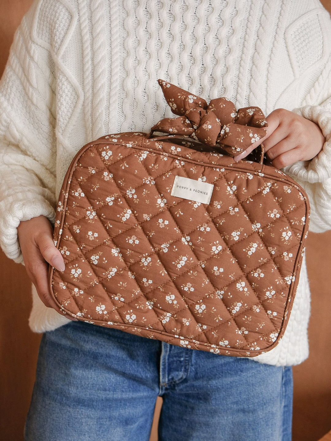 Lifestyle close-up of the Hook Me Up Cosmetic Case in Brown Floral, showcasing its roomy rectangular shape, quilted cotton finish, floral print, and top handle.