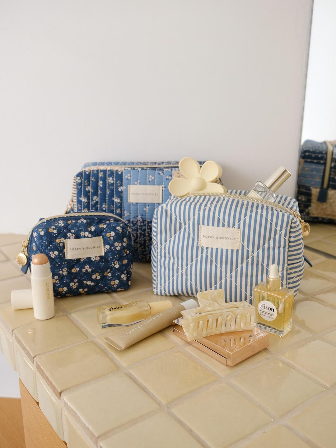 Product-focused lifestyle shot of the Cosmetic Trio in Navy Patchwork, featuring all three coordinating cosmetic cases in blue floral, striped, and patchwork prints styled alongside beauty essentials.