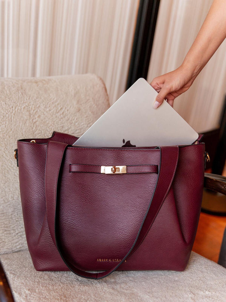 Berry coloured vegan leather tote bag with a laptop being placed inside, on a neutral background