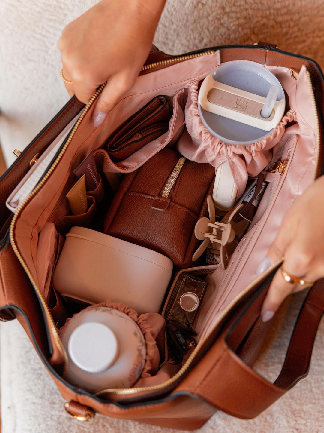 Open brown vegan leather tote bag with gold hardware full of accessories