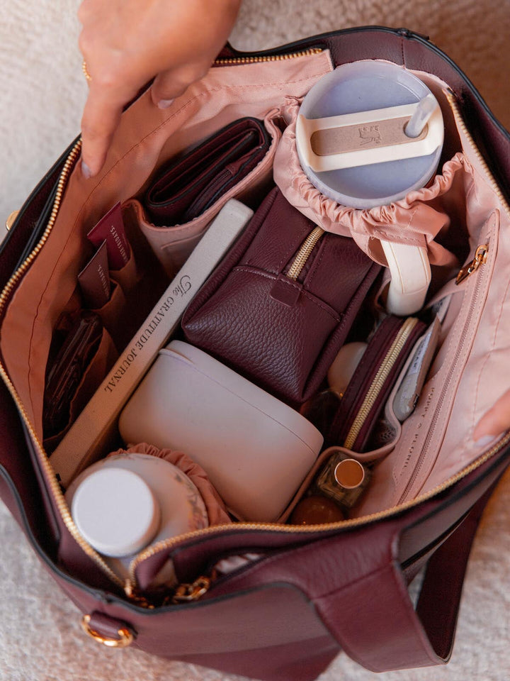 Open vegan leather handbag with various items including a wallet, phone, and makeup products.