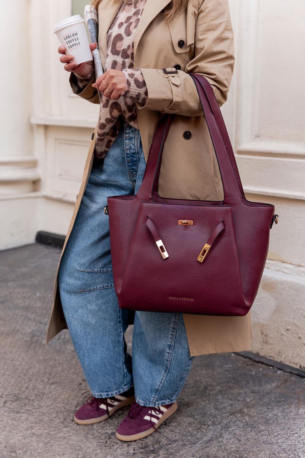 Woman holding a coffee and a berry coloured vegan leather tote bag with gold hardware