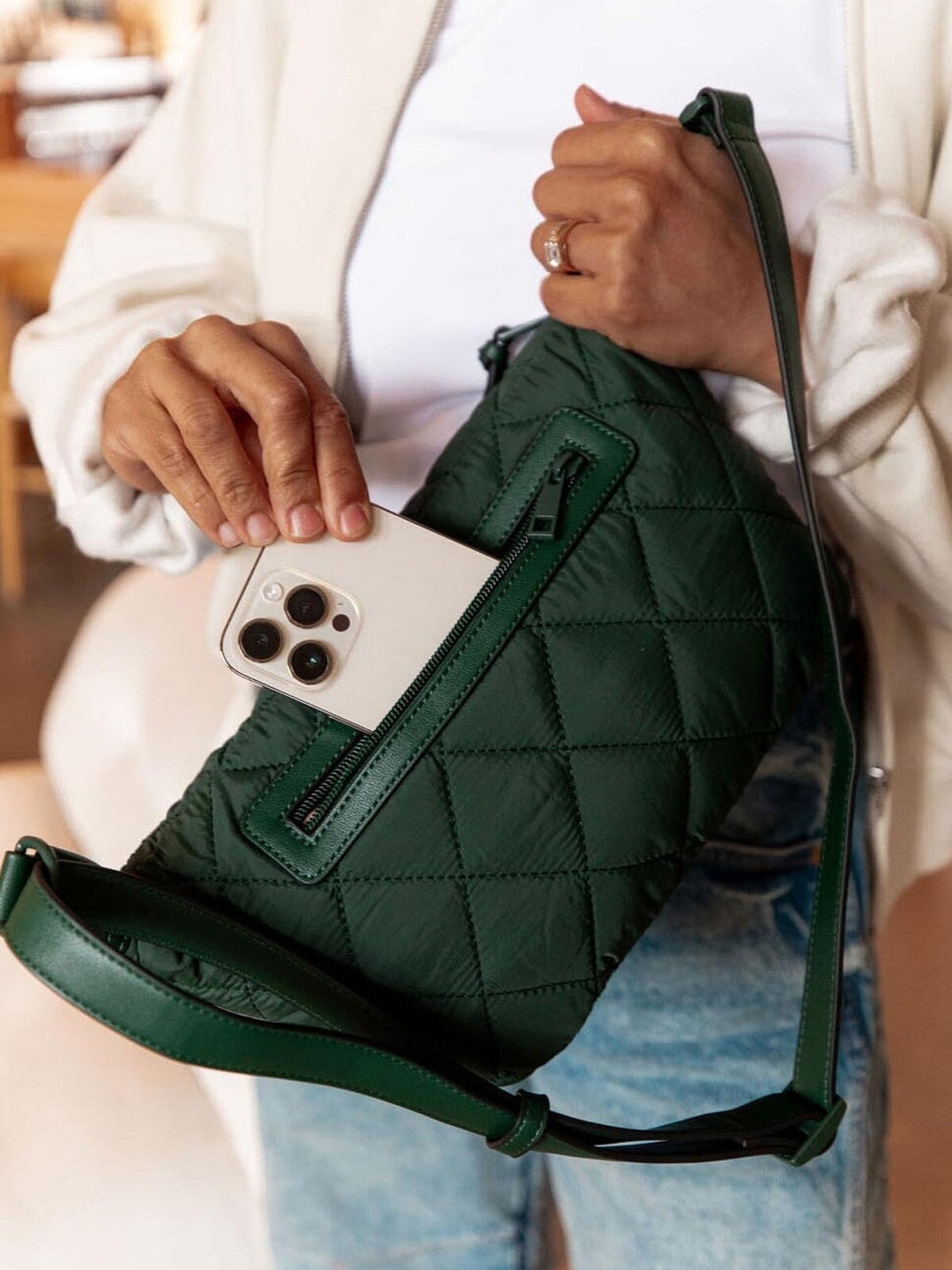 Green quilted bag with a phone inside, held by a person wearing a white sweater.