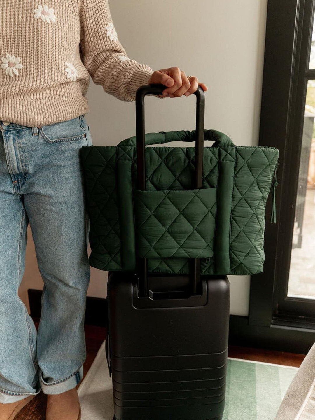 Person holding a green quilted tote bag over a black suitcase indoors.