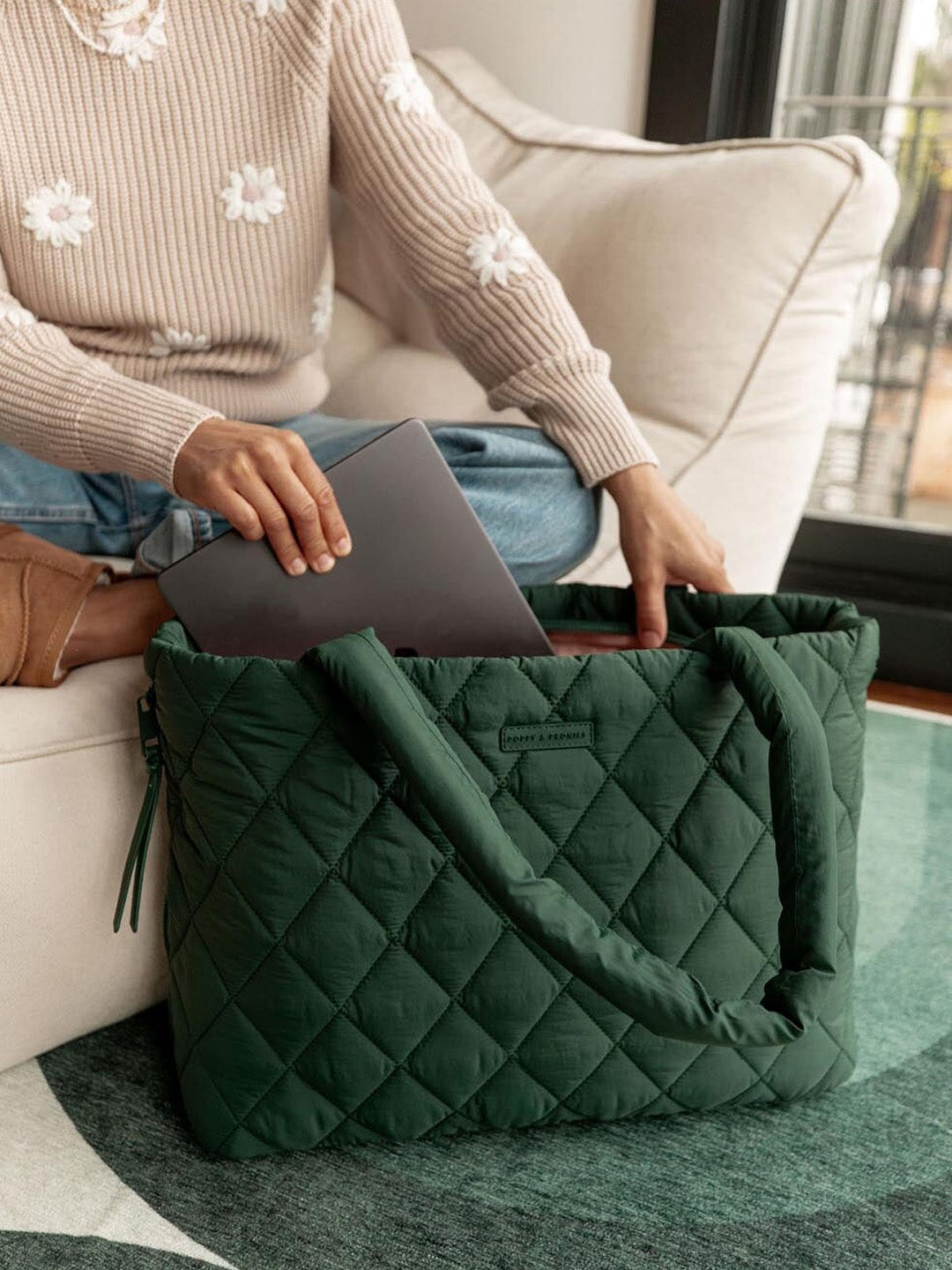 Person sitting on a couch with a green quilted tote bag and laptop