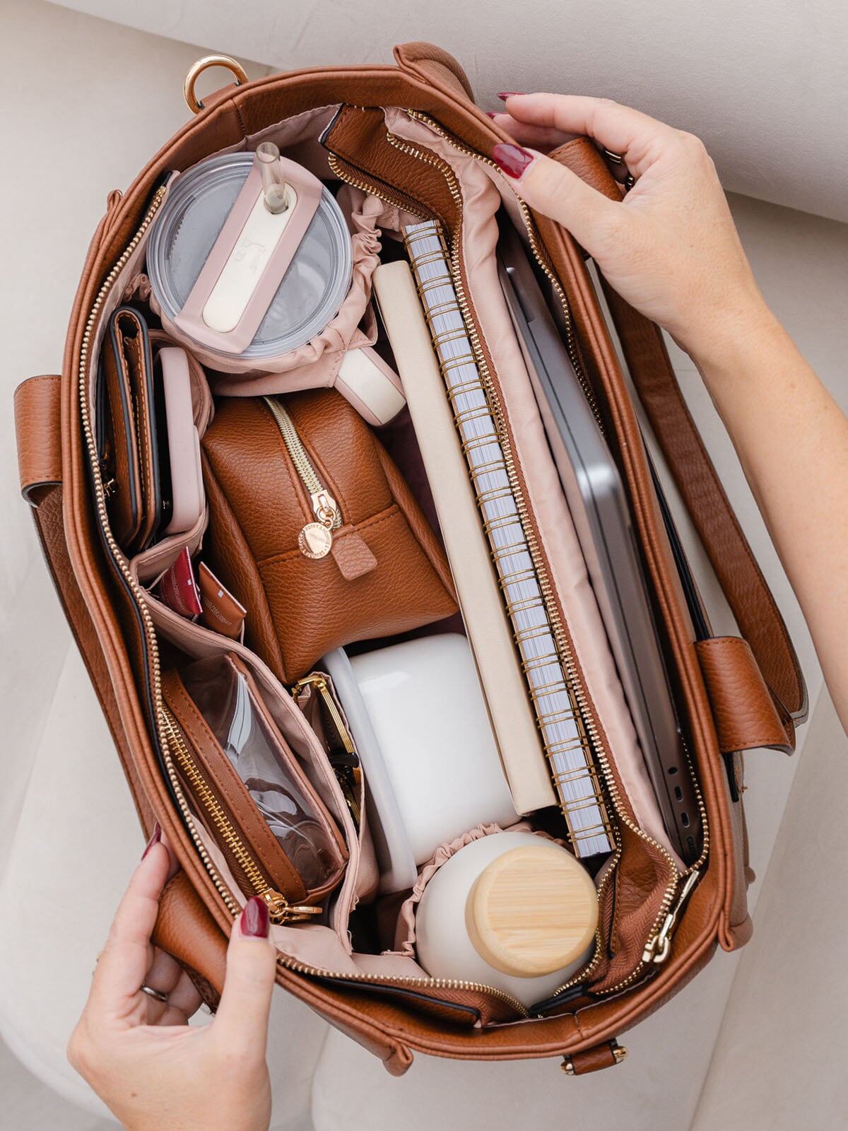 Brown vegan leather tote bag being opened to reveal its contents on a light background