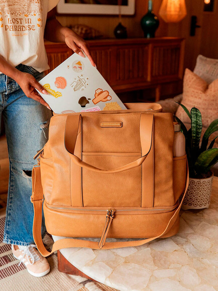 Person putting a laptop into a vegan leather travel bag in a cozy living room.
