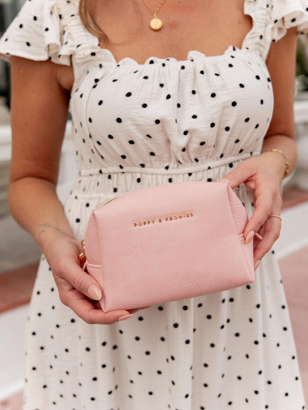 Person holding a pink vegan leather cosmetic case wearing a polka dot dress.