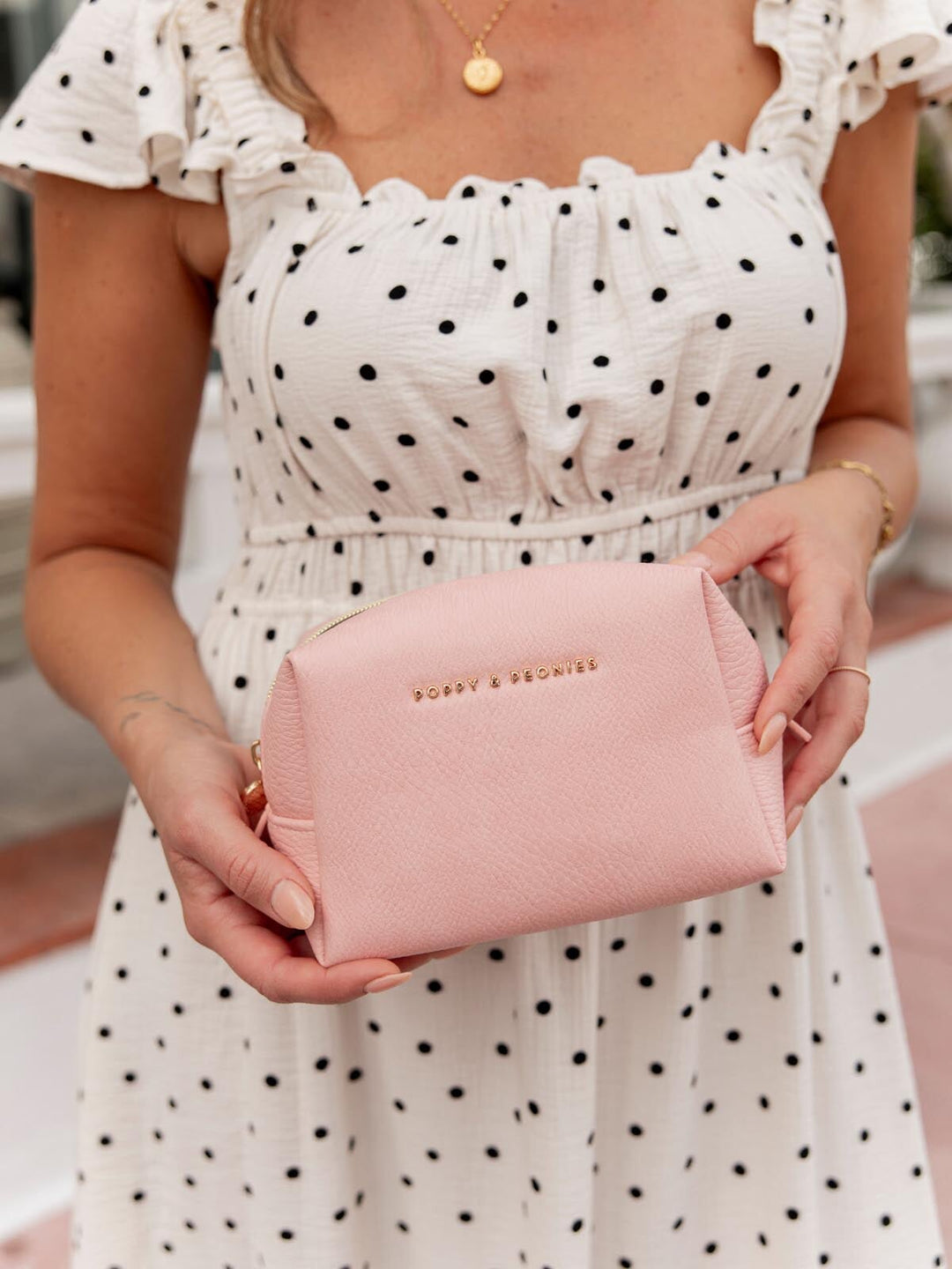 Person holding a pink vegan leather cosmetic case wearing a polka dot dress.