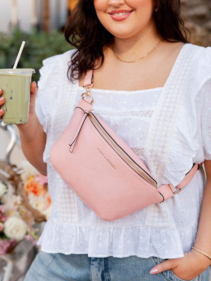 Woman wearing a pink crossbody bag, holding a drink, with a blurred outdoor background