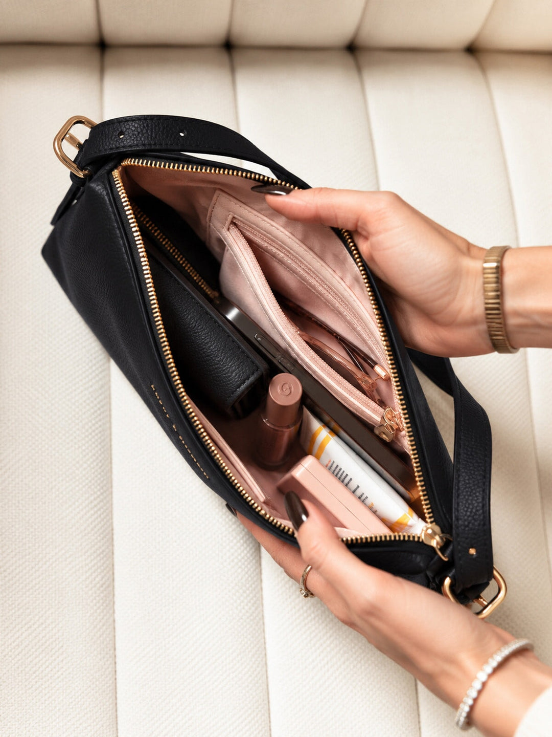 Poppy and Peonies The Soho Shoulder Bag Black featuring an open interior with blush pink lining, gold-tone zipper closures, an interior zippered pocket, and neatly arranged everyday essentials including a wallet, cosmetics, and personal accessories.